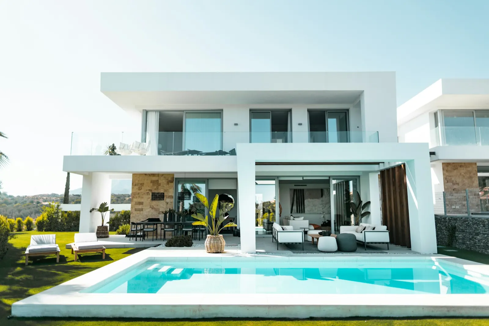 Önünde turkuaz havuz ve şezlonglar bulunan modern beyaz iki katlı villa